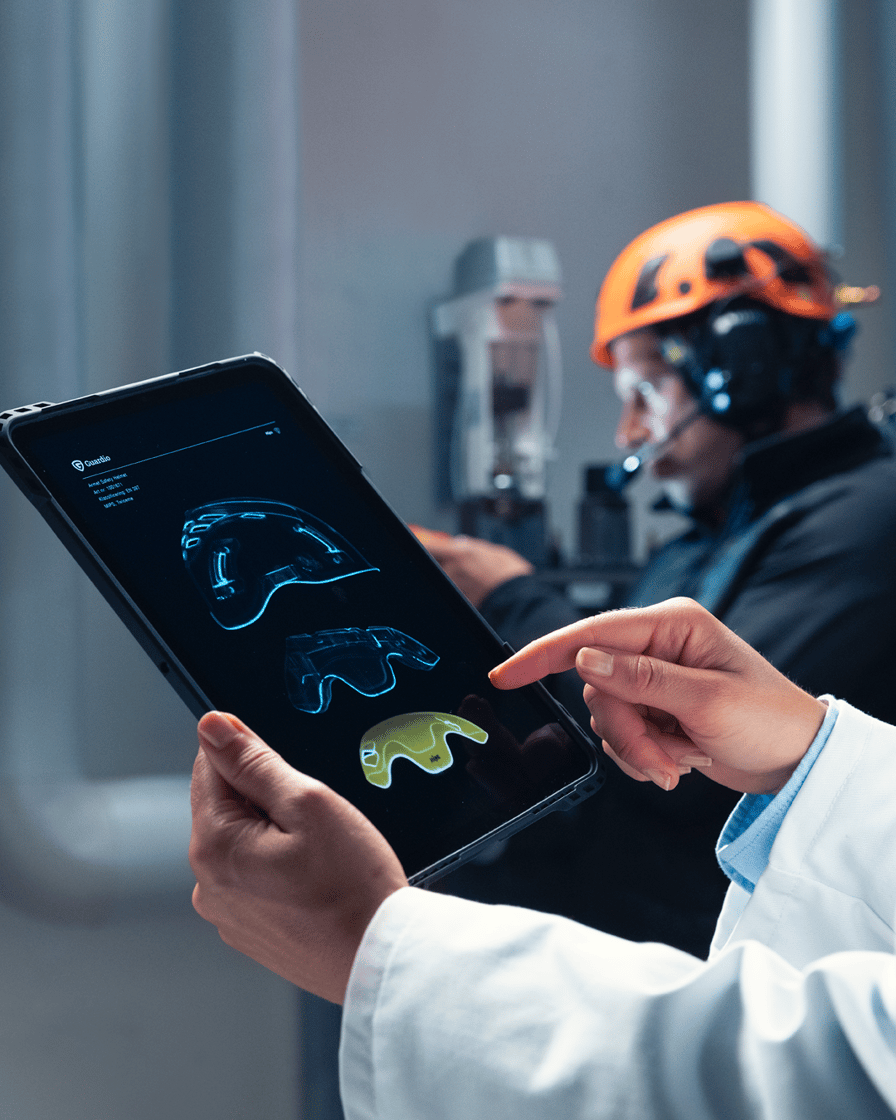Nahaufnahme eines Tablets, das die reibungsarmen Lager des Mips-Systems in einem Helm zeigt, mit Technikern im Hintergrund.